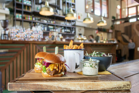Closeup of hamburgers with fries in a cup and sauce on a wooden tray with a blurred background